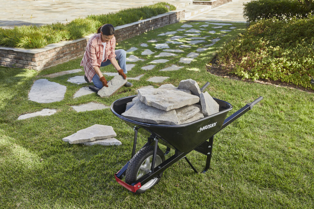 Man using a wheelbarrow to move rocks in a yard