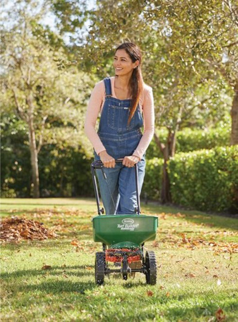 Woman using a lawn spreader on a yard