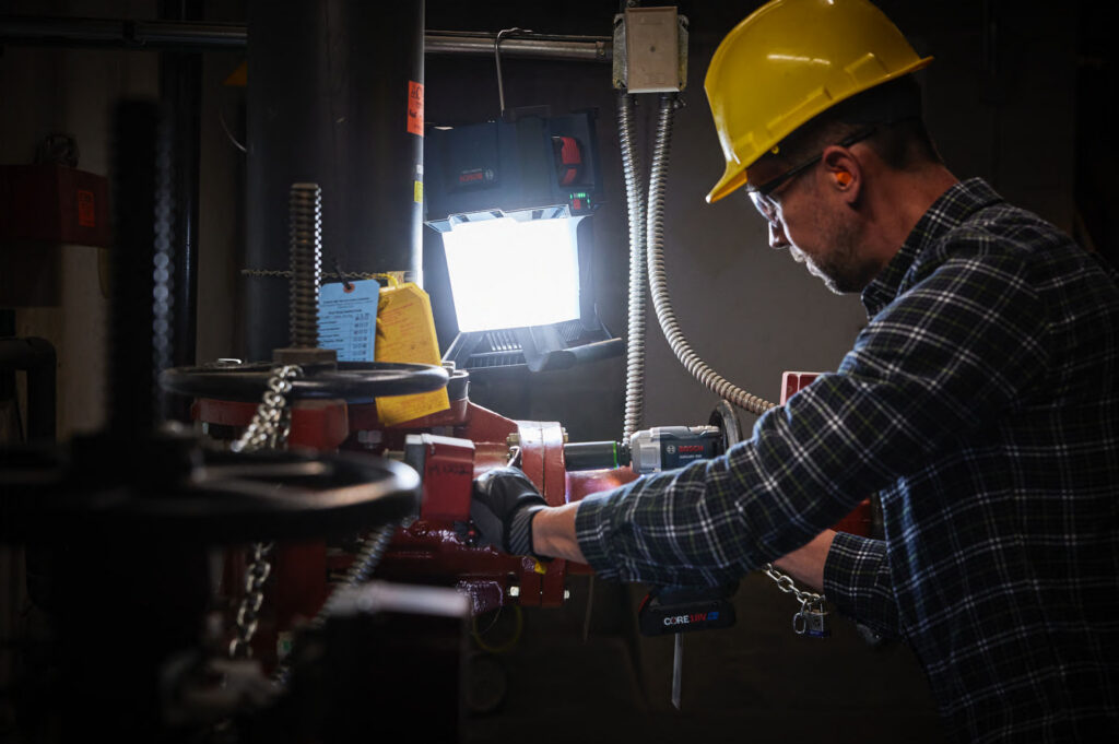 Man working at a workbench with a work light wearing a hard hat