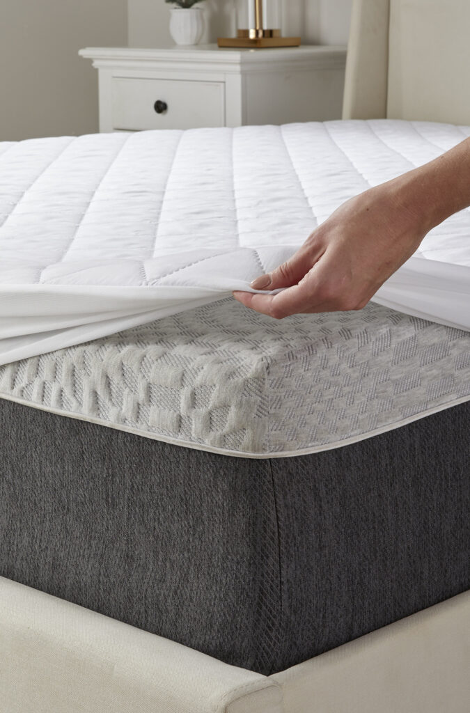 Person fitting a quilted mattress pad onto a bed