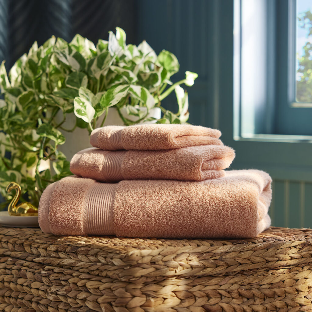 Folded tan towels on a woven basket with a plant